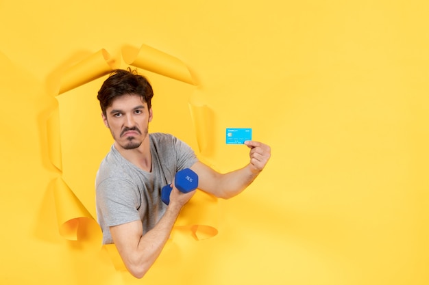 young male holding credit card and dumbbell on a yellow background workout fit athlete money