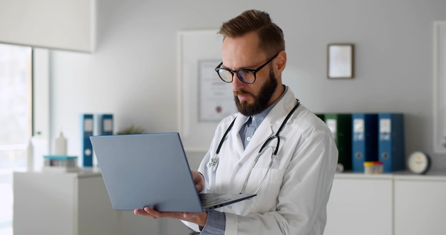 Young male hospital doctor working on laptop in office