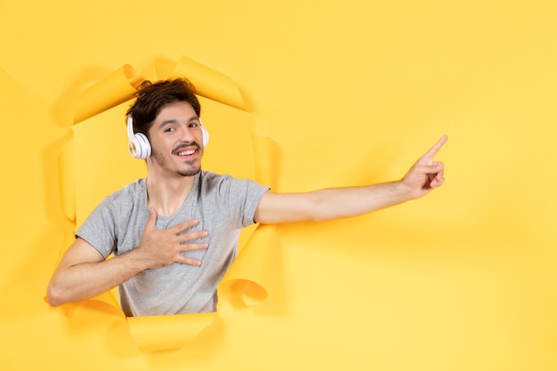 young male listening to music in headphones on yellow paper background sound audio