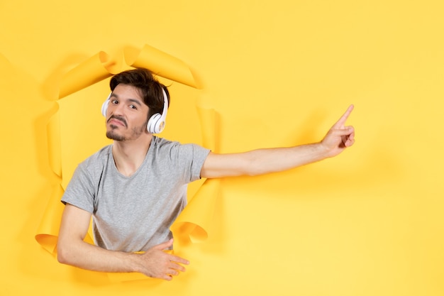 黄色い紙の背景音超音波でヘッドフォンで音楽を聴いている若い男性