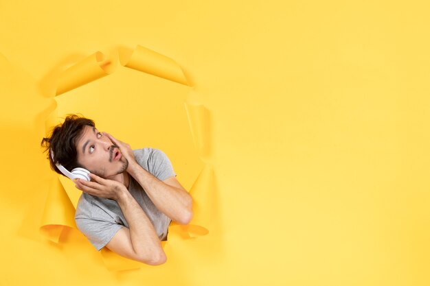 young male listening to music in headphones on yellow paper surface sound ultrasound audio