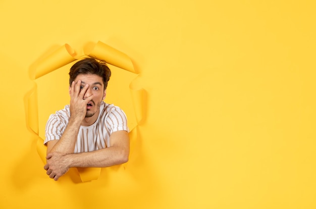 Young male looking and standing on the torn yellow paper background facial indoor guy sale