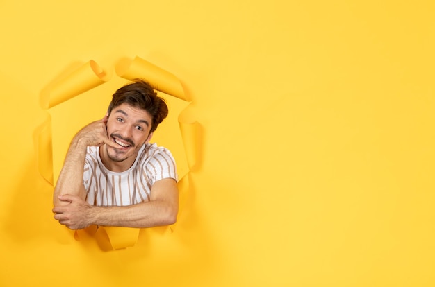 Young male looking and standing on torn yellow paper background guy facial indoor