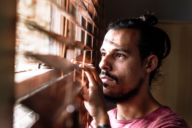 A young male looking through the window blinds to stay safe during Coronavirus outbreak