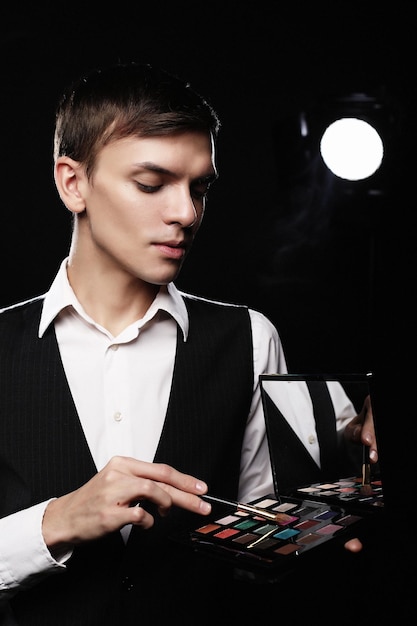 Young male make up artist holding shadow palette and brush