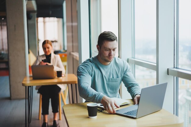 A young male manager sits in an office with large windows and\
works at a laptop a handsome businessman is working on his homework\
in a cafe