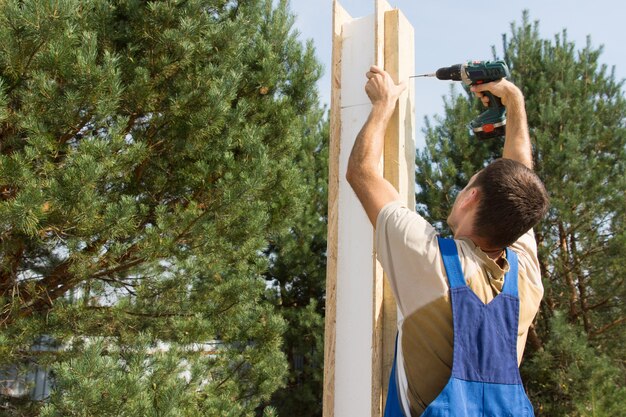 Young Male Manual Worker Drilling a Wooden Post at the Construction Site.