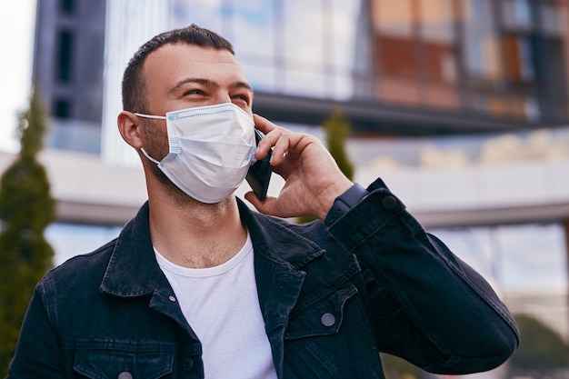 Foto giovane maschio in maschera che risponde a una telefonata in città