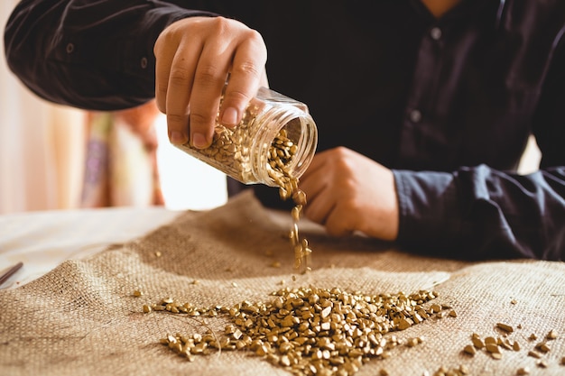 Young male miner sitting at table and pouring gold out of glass jar