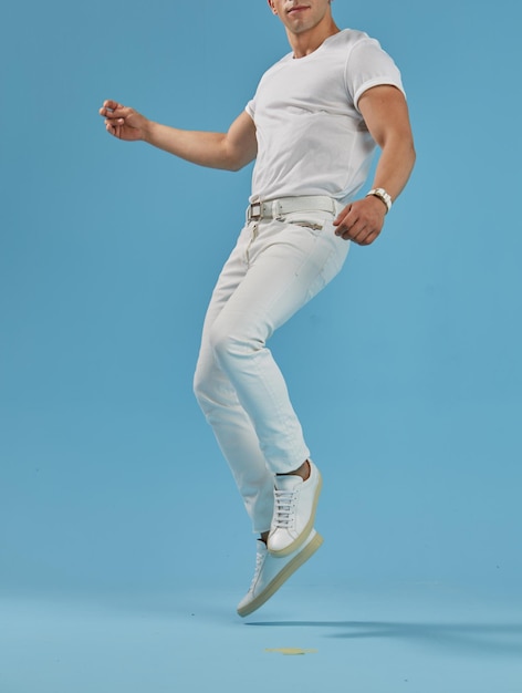 Young male model with white casual shirt and jeans dancing in front of a blue background