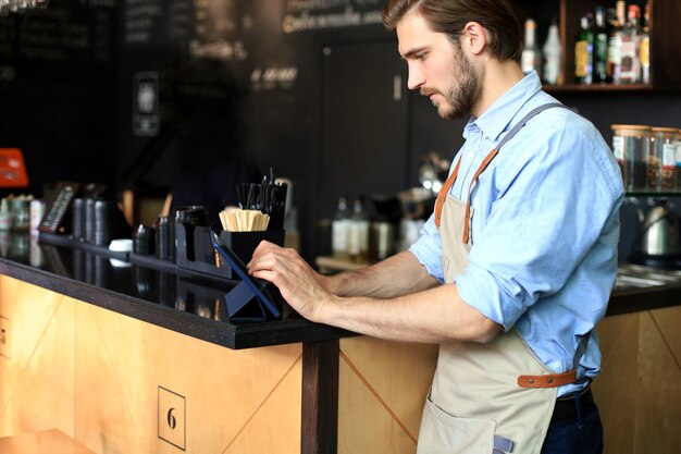 Young male owner using digital tablet while standing in cafe.