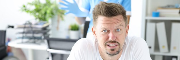 Young male patient lies on couch on stomach with doctor wearing rubber glove in background