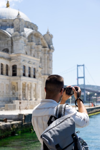 Молодой фотограф-мужчина фотографирует Босфорский мост и мечеть Ортакёй в Стамбуле