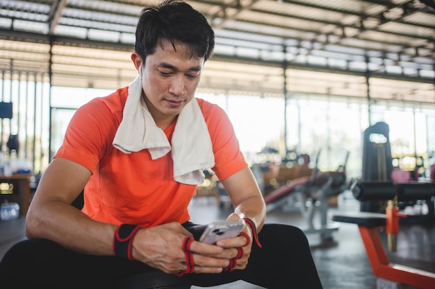 Foto giovane maschio che gioca al telefono e ascolta musica dopo l'esercizio con varie attrezzature per l'esercizio fisico