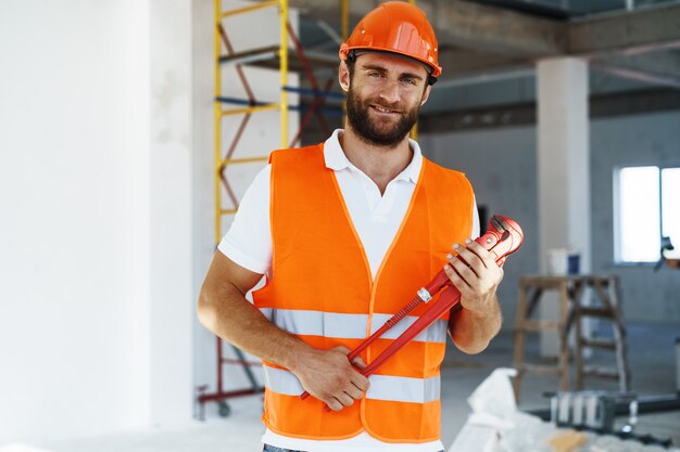 Young male plumber holding pipe wrench on a construction site indoors