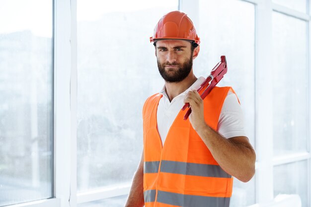 Young male plumber holding pipe wrench on a construction site indoors