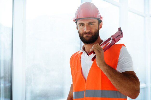 Young male plumber holding pipe wrench on a construction site indoors