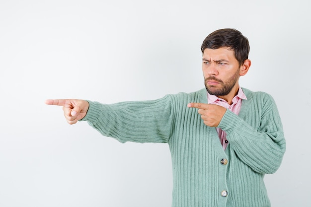 Young male pointing aside in shirt, cardigan and looking confident , front view.