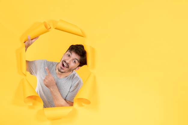 young male pointing above on torn yellow paper background indoor handsome facial