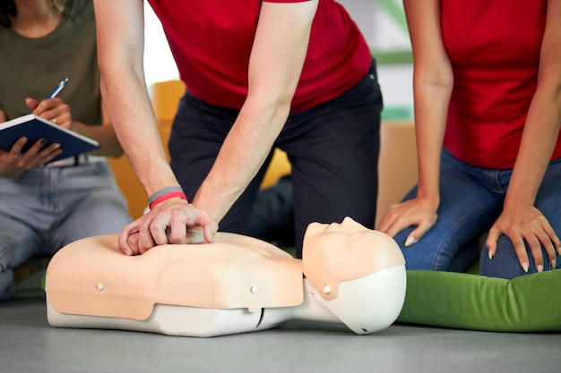 Photo young male practicing cpr first aid on a mannequin in the presence of people