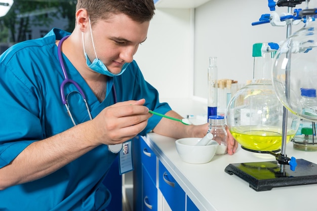 Young male scientist in uniform wearing a mask preparing powder on ceramic plate for some research in a laboratory. Healthcare and biotechnology concept