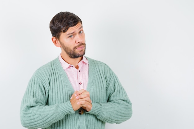 Young male in shirt, cardigan with hands clasped and looking pensive , front view.