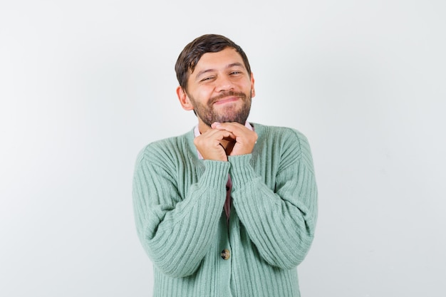 Young male in shirt, cardigan with hands in pleading gesture and looking ashamed , front view.