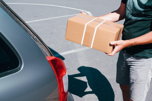 Young male shopper stacks cardboard boxes in the trunk of a car in a supermarket parking lot Closeup view