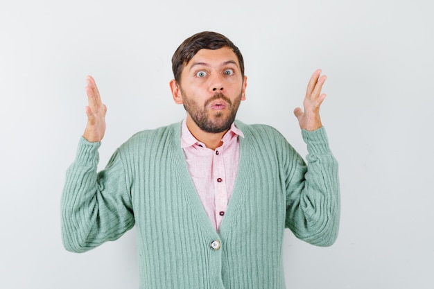 Young male showing large size sign in shirt, cardigan and looking wondered , front view.