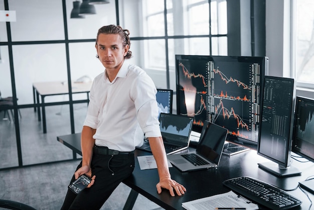 Young male stock brocker works indoors in the office Many of displays