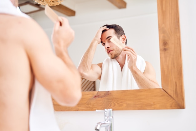 Young male stroking his hair while standing by mirror