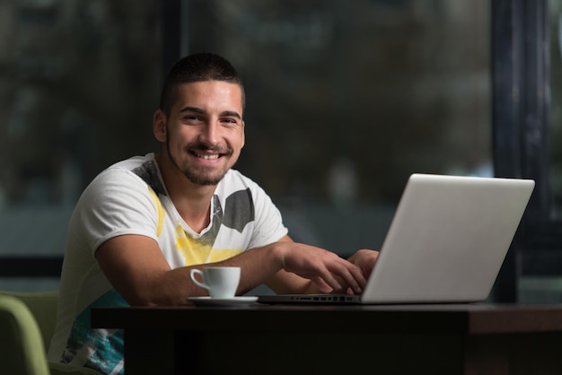 Молодой студент мужского пола пьет и развлекается с ноутбуком в кафетерии