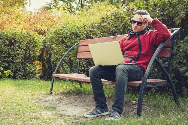 Young male student programmer work study outdoors. Programmer developer works with his laptop in the Park outside the office. Pensive man with an ultrabook on a bench.