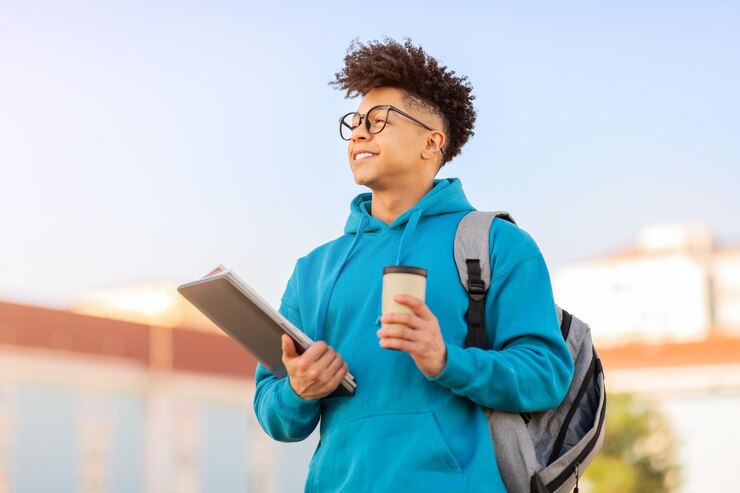Photo young male student standing outdoors with laptop and takeaway coffee