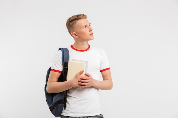 Zaino da portare del giovane studente maschio che esamina da parte copyspace con sguardo meditabondo mentre tenendo i libri isolati su bianco