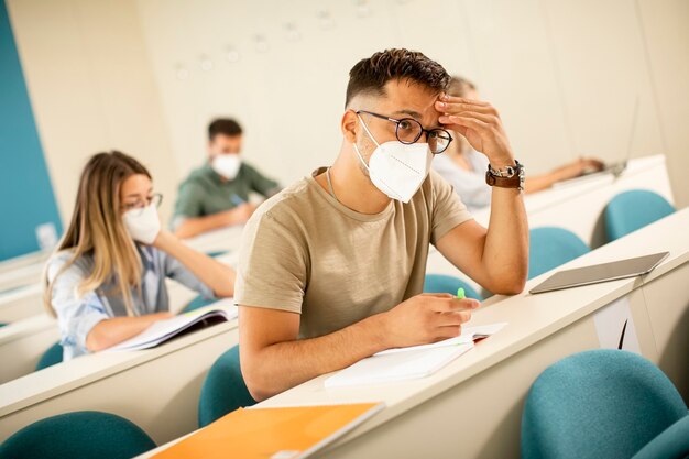 講堂でウイルス対策のための顔面保護医療マスクを身に着けている若い男子学生