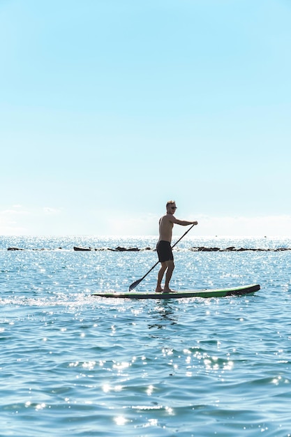 海でスタンドアップパドルボードに乗る若い男性サーファー