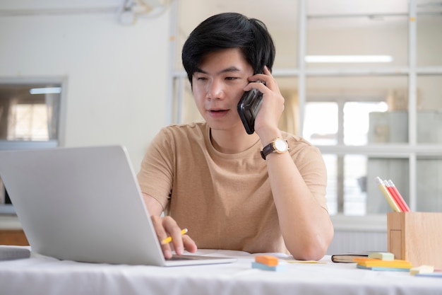 携帯電話で話しているとラップトップに取り組んでいる若い男性