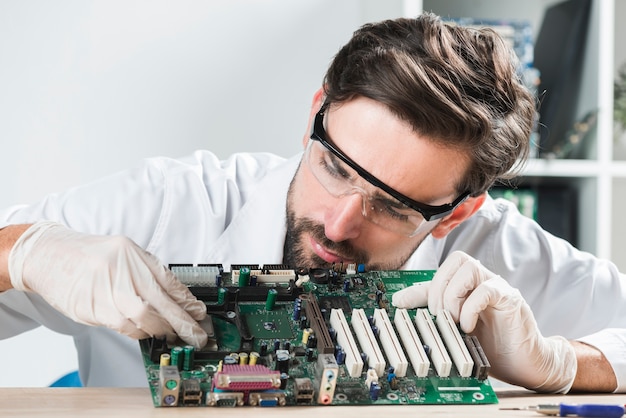 Foto giovane tecnico maschio che inserisce chip nella scheda madre del computer sullo scrittorio di legno