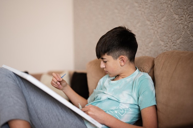 Молодой мужчина-подросток рисует картину по номерам на холсте в гостиной дома Хобби и отдых c