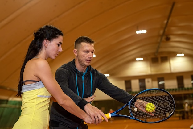 Young male tennis player teaches a woman to play tennis on the court