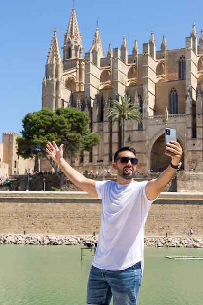 Young male tourist photographing himself in front of the cathedral of Palma de Mallorca on a sunny day in Spain