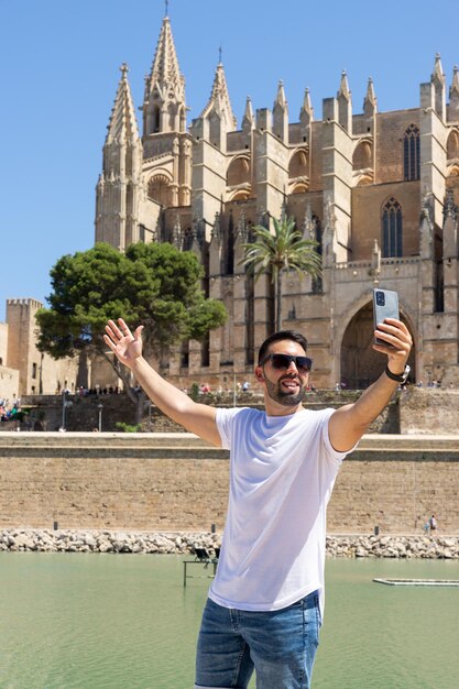 Молодой турист-мужчина фотографирует себя перед собором пальма-де-майорка в солнечный день в испании
