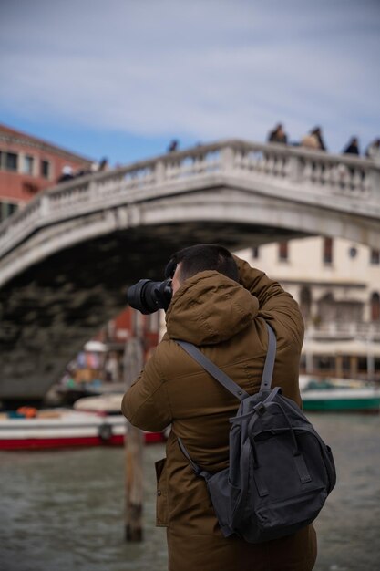 写真 ヴェネツィアの運河を写真撮影する若い男性観光客