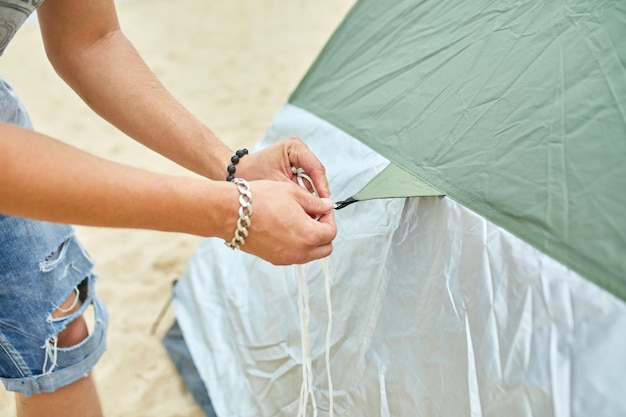 Young male tourist puts a green tent in the beach coast The man sets up a camp on a hike