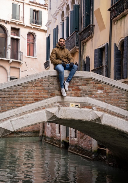 Young male tourist sitting on a bridge at a canal crossing in Venice