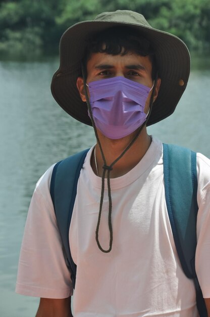 Foto un giovane turista di sesso maschile che indossa una maschera facciale guardando la telecamera mentre si trova accanto al lago