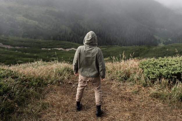 A young male traveler stands on the top of the mountain with his hands down and looks at the place for the text. Tourism concept. Copy space