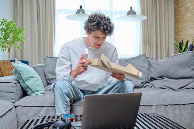 Young male unpacking an online purchase with box with new smartphone