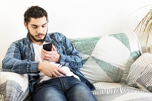 Young male using a smart phone sitting on the couch in the living room at home